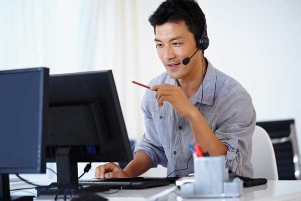 A man working at a computer while also on the phone