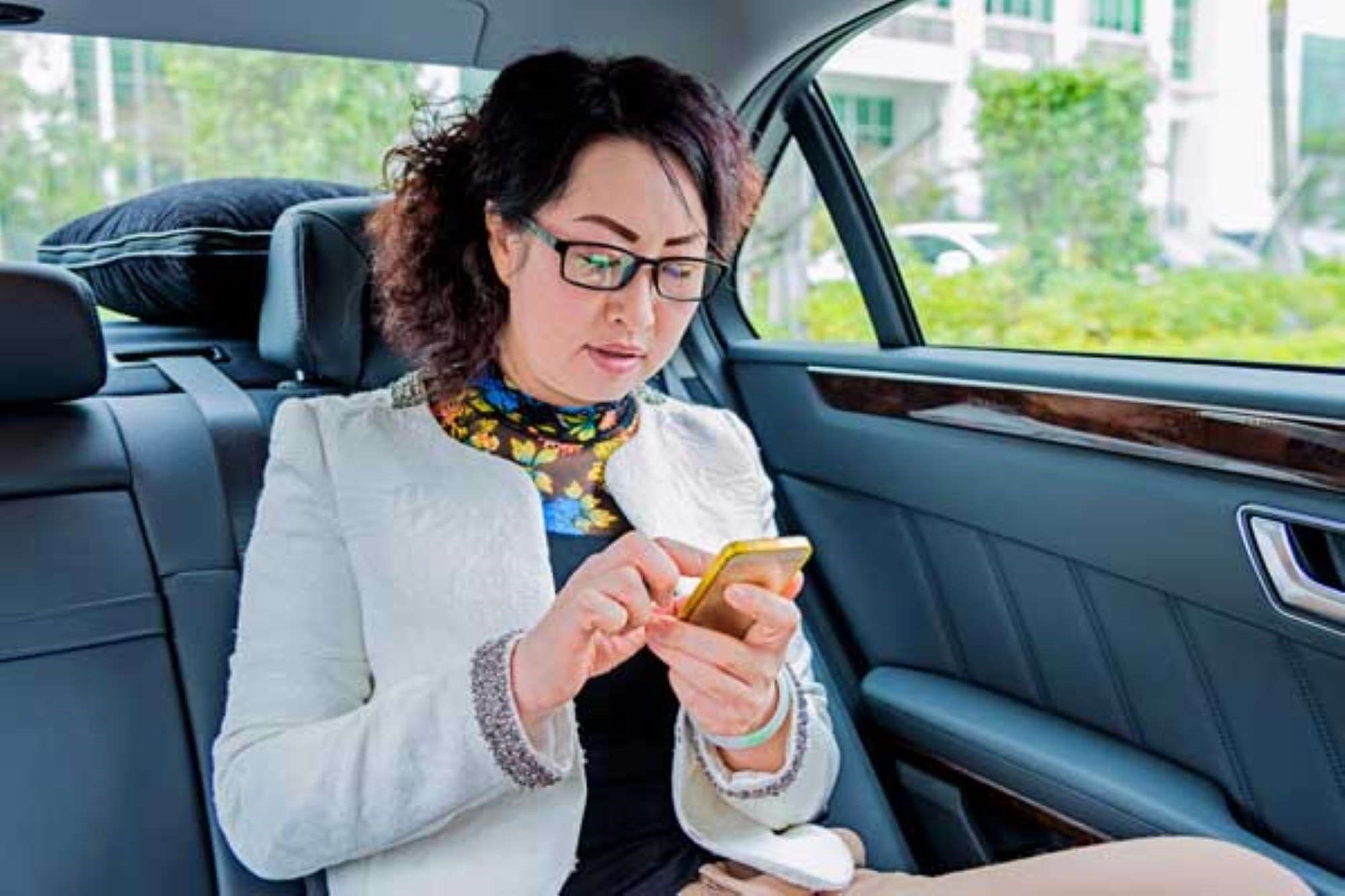 A lady using her phone in the back of a car
